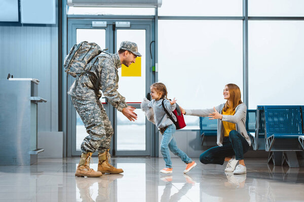 happy daughter running to father in military uniform in airport 