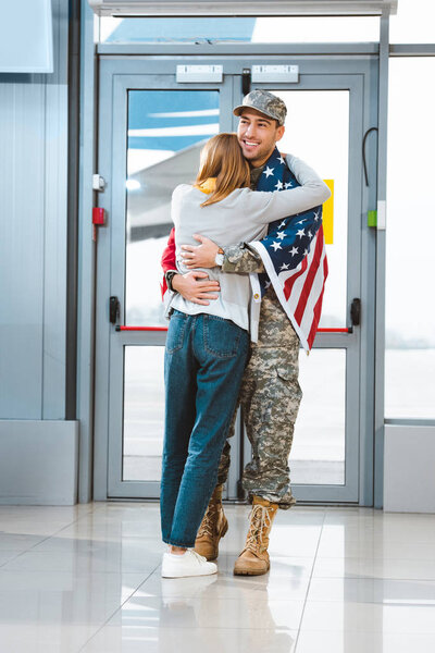 cheerful veteran in military uniform hugging girlfriend in airport 
