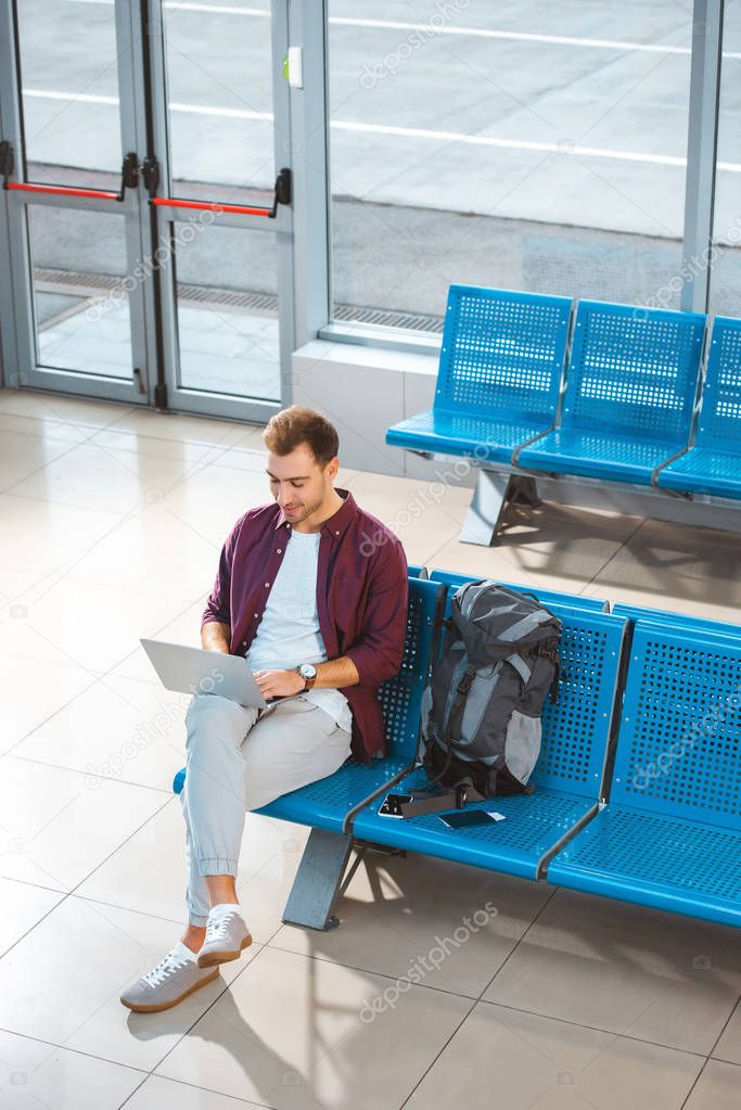 overhead view of handsome man using laptop while sitting in waiting hall