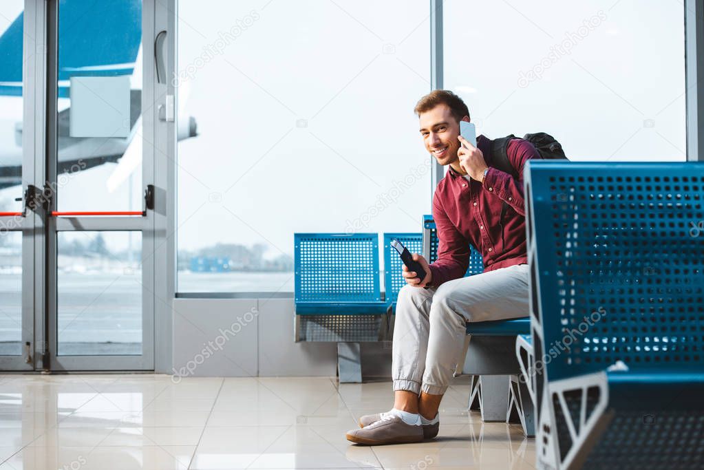 cheerful man talking on smartphone while sitting in departure lounge