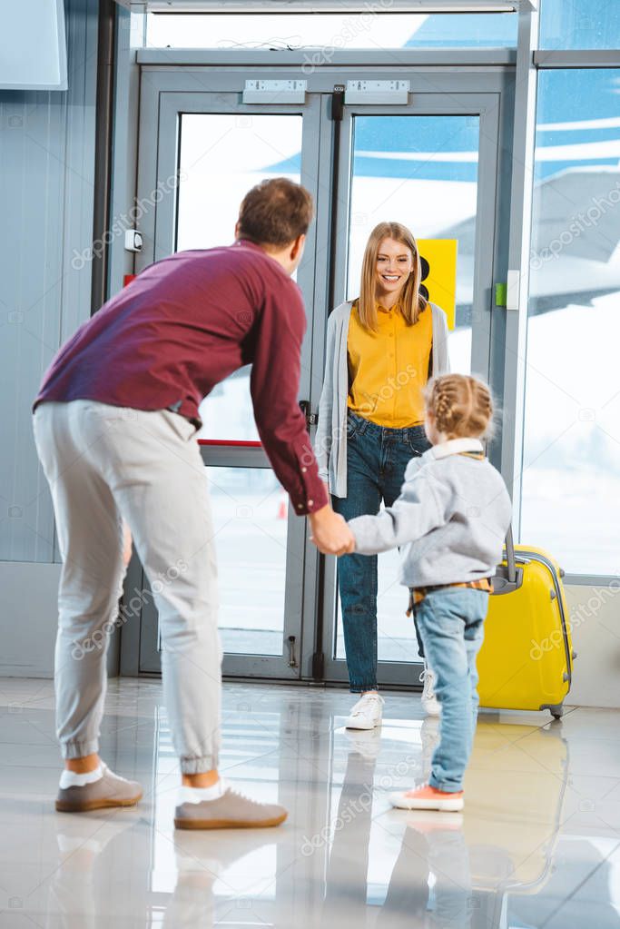 cheerful mother looking at daughter and husband holding hands in airport 