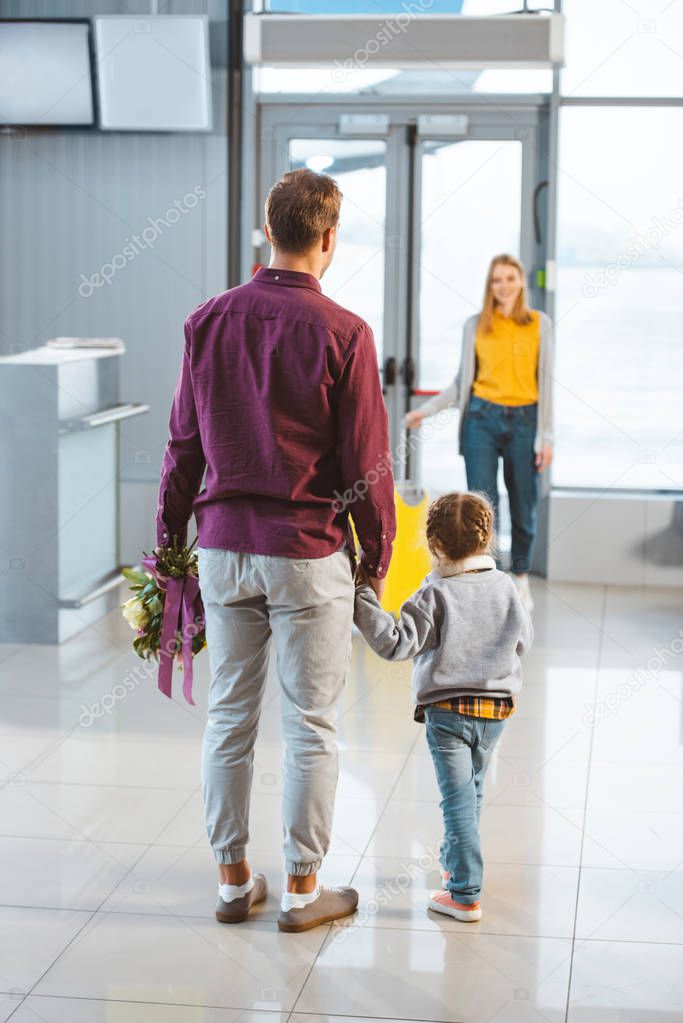 selective focus of man holding hands with daughter and looking at wife with luggage 