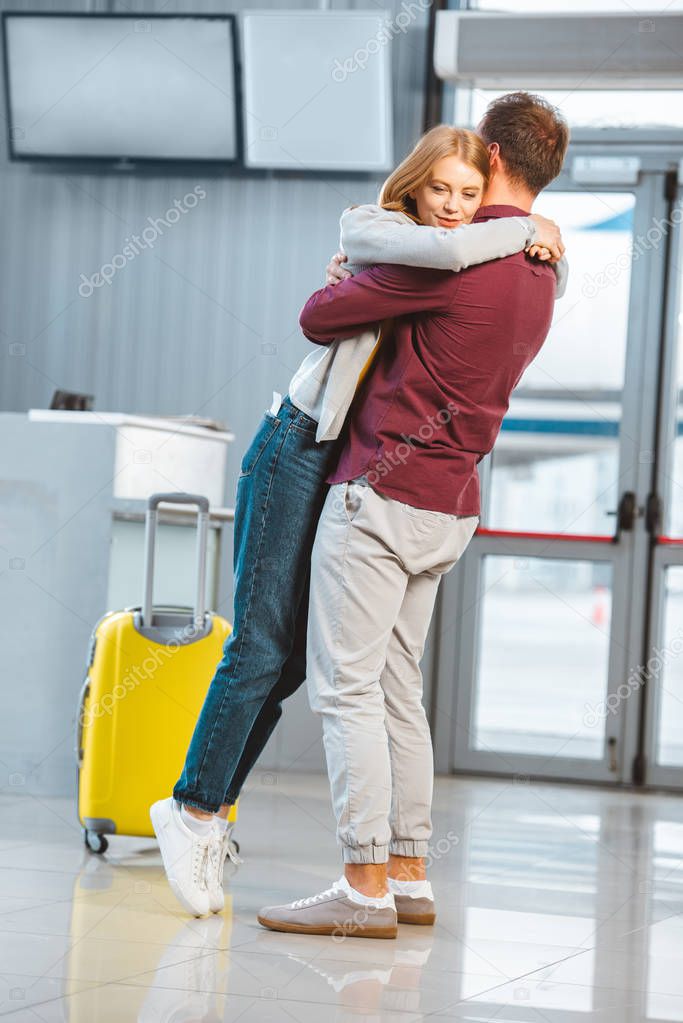 beautiful woman hugging boyfriend in waiting hall near luggage 