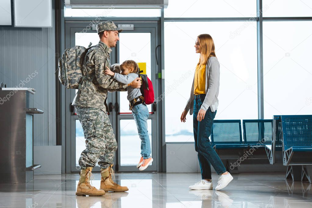 happy father in military uniform holding in arms daughter near wife in airport 