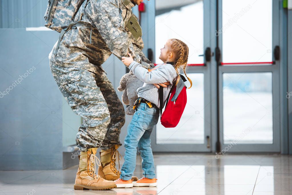 happy daughter holding father in military uniform in airport 