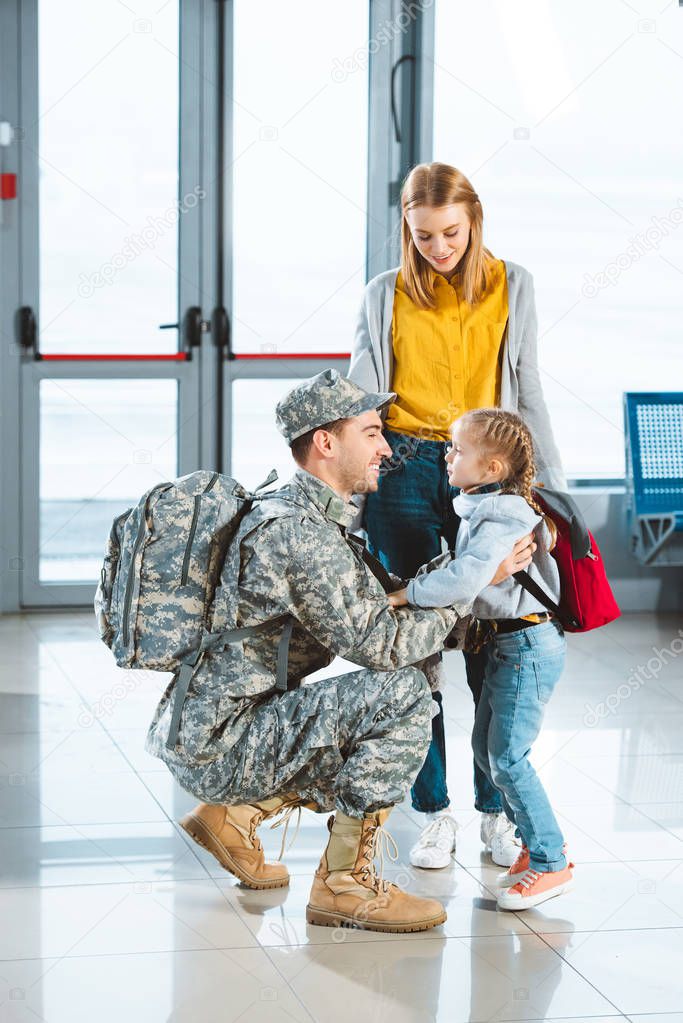 cheerful dad in military uniform hugging daughter near wife in airport 