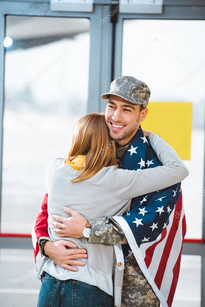 back view of woman hugging boyfriend in military uniform with american flag in airport 