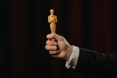 KYIV, UKRAINE - JANUARY 10, 2019: cropped view of man holding oscar award on dark background clipart