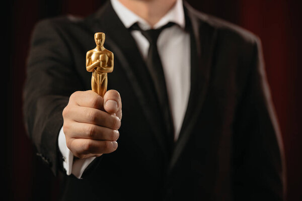 КИЕВ, УКРАИНА - 10 ЯНВАРЯ 2019 года: избирательное внимание мужчины в костюме, держащего Оскар награду на тёмном фоне