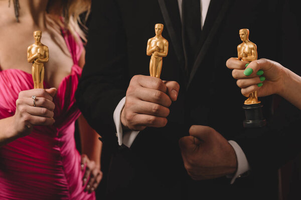 KYIV, UKRAINE - JANUARY 10, 2019: cropped view of women and man holding oscar awards isolated on black