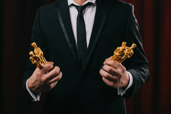 KYIV, UKRAINE - JANUARY 10, 2019: partial view of man in suit holding oscar awards on dark background
