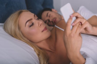 güzel şüpheli kadın yatakta uyuyan koca, gizli kavramı ile yalan sırasında Smartphone kullanarak