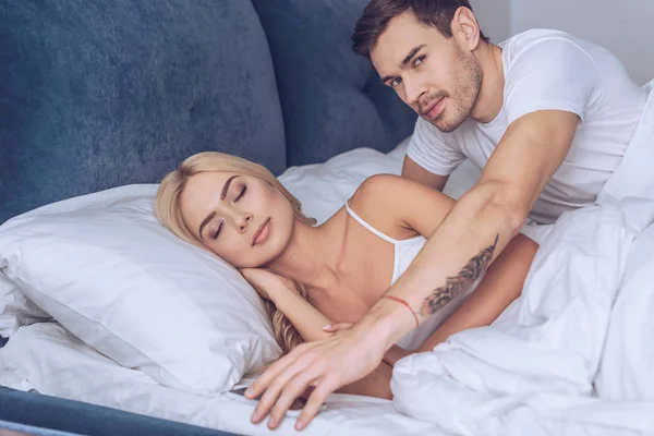 Young Man Reaching Smartphone Looking Camera While Girlfriend Sleeping Bed — Stock Photo, Image