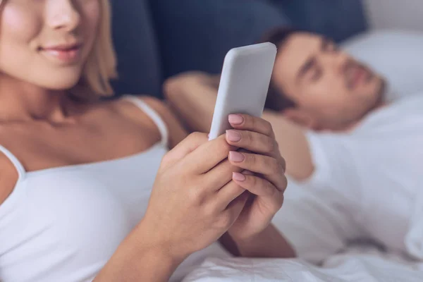 Corte Tiro Sorrir Jovem Mulher Usando Smartphone Enquanto Marido Dormindo — Fotografia de Stock