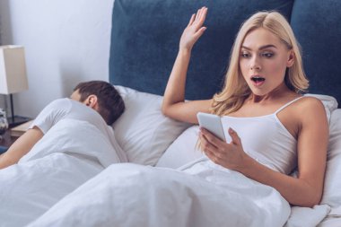 şok genç kadın yatakta uyuyan koca ise Smartphone kullanarak