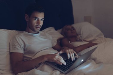 dizüstü bilgisayar kullanarak ve karısı yatakta gece uyku sırasında kamera bakarak şüpheli genç adam 