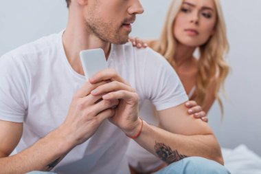 smartphone ve kız arkadaşı arkasında yatak odasında bakmak kullanan adam resmini kırpılmış, güvensizlik kavramı