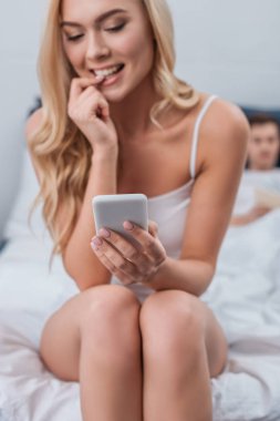 gülümseyen tırnak ısırma ve yatakta yatan koca ise smartphone kullanarak genç kadın 