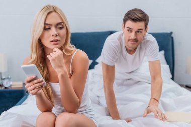 Smartphone ve kıskanç koca arkasında yatağa atmayı kullanan genç kadın