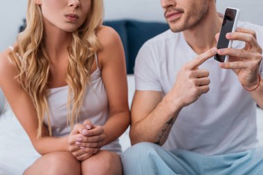 kıskanç erkek genç kadın yatakta oturuyordu smartphone vasıl işaret kadeh kırpılmış, güvensizlik kavramı