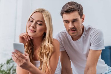 gülümseyen kız yatak odasında smartphone kullanarak bakarak kıskanç genç adam