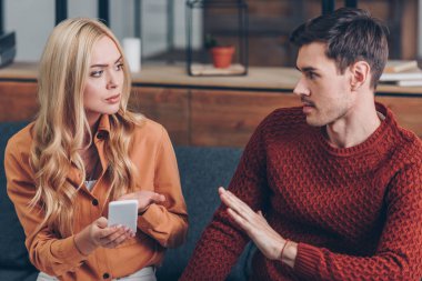 young couple quarreling about smartphone and looking at each other, relationship problem concept clipart