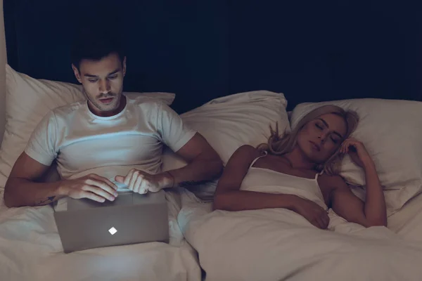 Suspicious Young Man Using Laptop While Beautiful Girlfriend Sleeping Bed — Stock Photo, Image