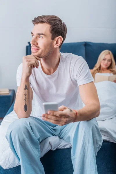 Pensive Man Sitting Hand Chin Using Smartphone While Girlfriend Reading — Stock Photo, Image