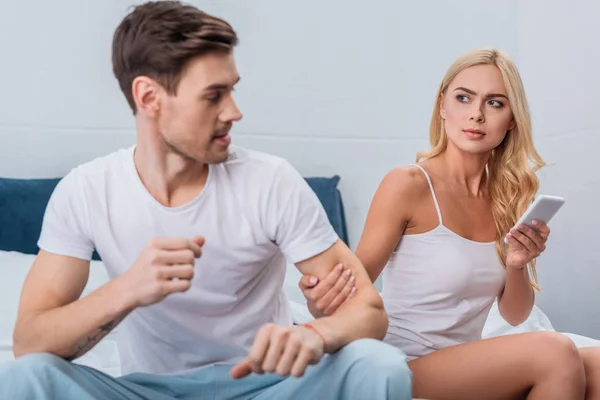 Young Woman Using Smartphone Looking Angry Boyfriend Sitting Bed Distrust — Stock Photo, Image