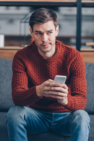 Nadenkend Jonge Man Houden Smartphone Zoek Weg Zittend Bank Thuis — Stockfoto