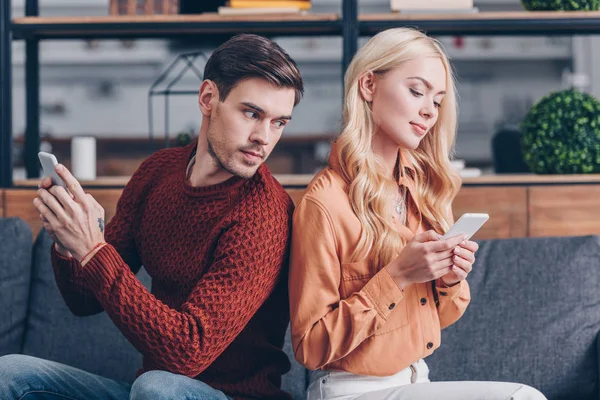 年轻夫妇背靠背坐着 并使用智能手机 嫉妒的概念 — 图库照片