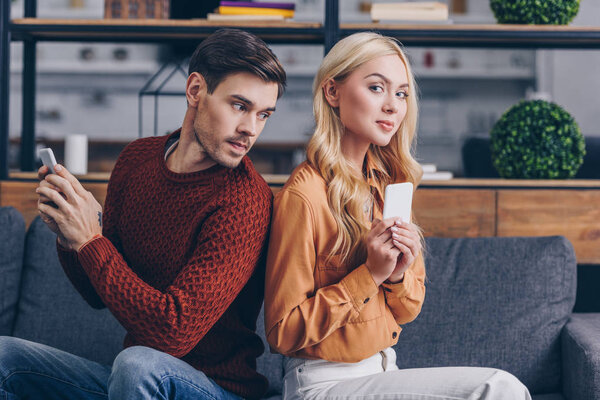 молодая пара сидит спиной к спине и с помощью смартфонов, концепция недоверия
 