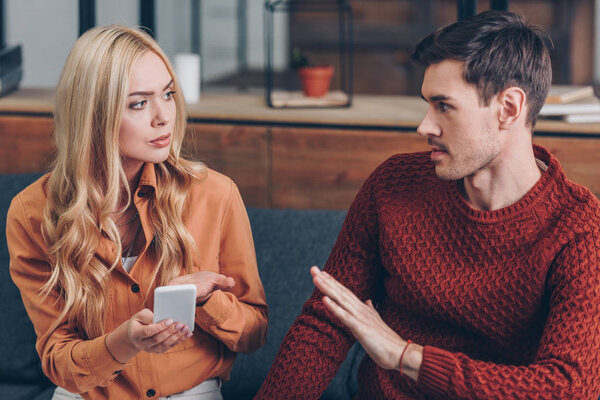 young couple quarreling about smartphone and looking at each other, relationship problem concept
