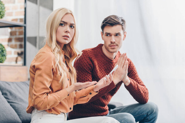 Молодой человек смотрит на шокированную девушку, держащую смартфон и смотрящую в камеру, концепцию недоверия
