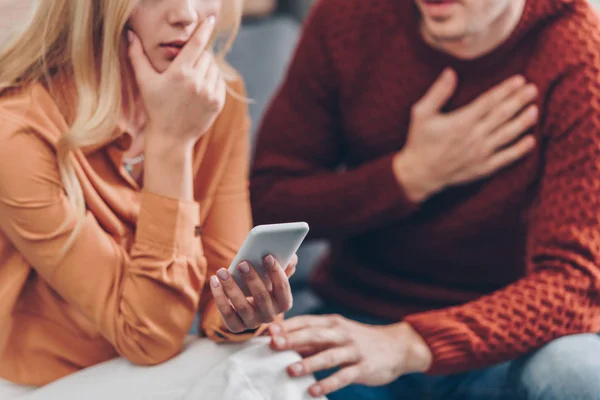 Corte Tiro Mulher Chocada Segurando Smartphone Homem Confuso Sentado Perto — Fotografia de Stock