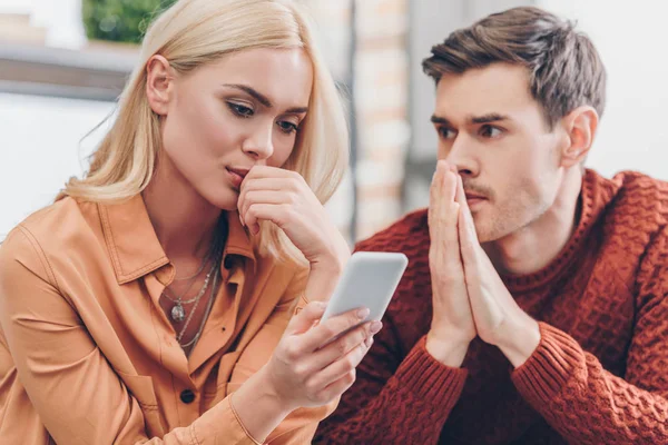 Jovem Olhando Para Namorada Usando Smartphone Casa Conceito Desconfiança — Fotografia de Stock