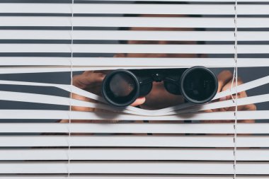 suspicious young man with binoculars spying through blinds clipart