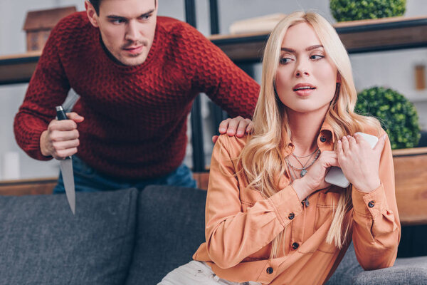 агрессивный мужчина с ножом глядя на девушку с помощью смартфона дома, концепция недоверия
 