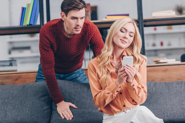 Namorado Olhando Para Bela Namorada Sorridente Usando Smartphone Casa Conceito — Fotografia de Stock