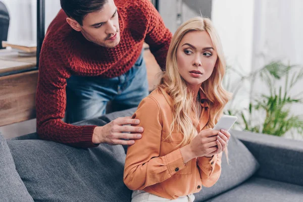 Jealous Husband Looking Scared Young Woman Using Smartphone Couch Distrust — Stock Photo, Image