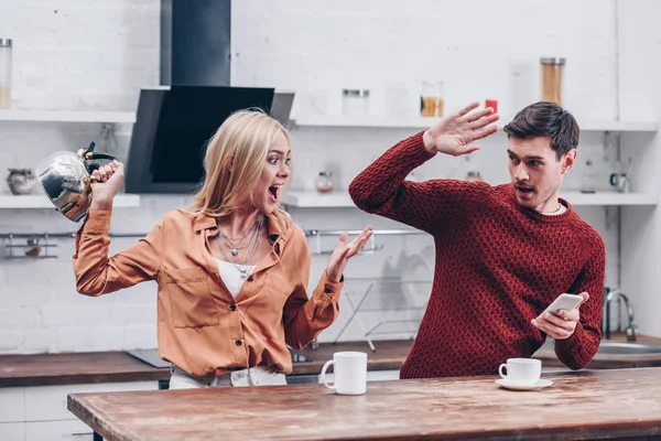 Angry Young Woman Kettle Yelling Husband Smartphone Kitchen — Stock Photo, Image