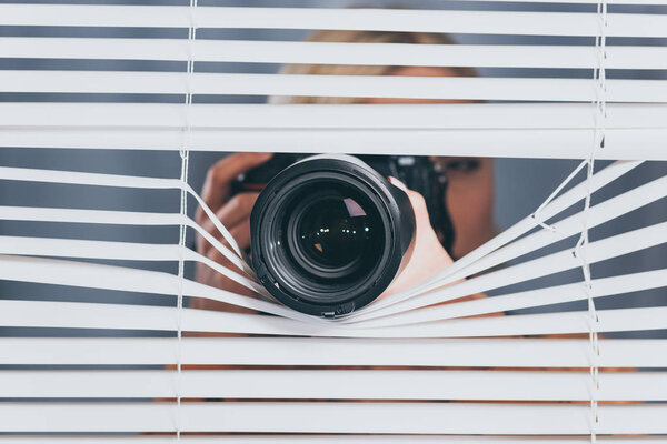 young woman photographing with camera and spying through blinds