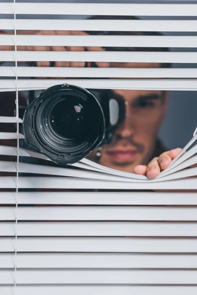 Visão Perto Jovem Segurando Câmera Olhando Para Câmera Através Persianas — Fotografia de Stock