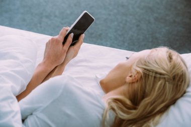 Yalnız kadın yatakta yatan ve smartphone ile boş ekran kullanma