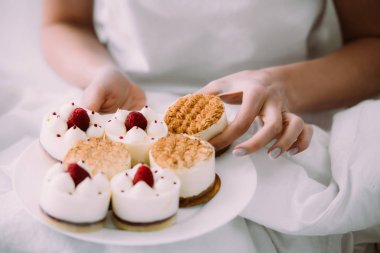 cropped view of woman holding one of cakes on plate in bed  clipart