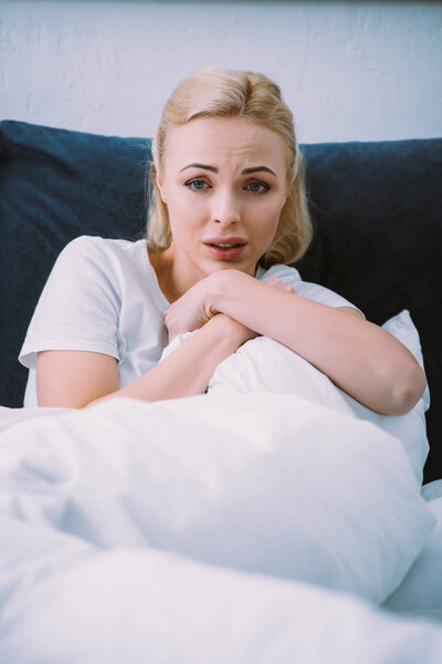 selective focus of scared woman holding blanket in bed at home