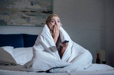 korkmuş kadın evde yatakta tv izlerken el ağzıyla kapsayan