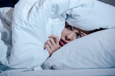 scared woman hiding behind blanket in bedroom at home clipart