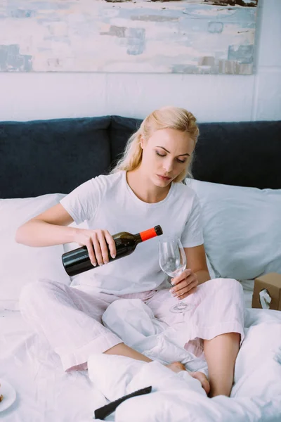 悲伤的女人在睡衣浇灌葡萄酒在床上在家里 — 图库照片
