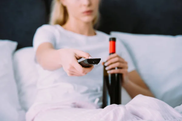 家でテレビを見ながらワインとリモコンのボトルを保持しているパジャマの女性観をトリミング — ストック写真